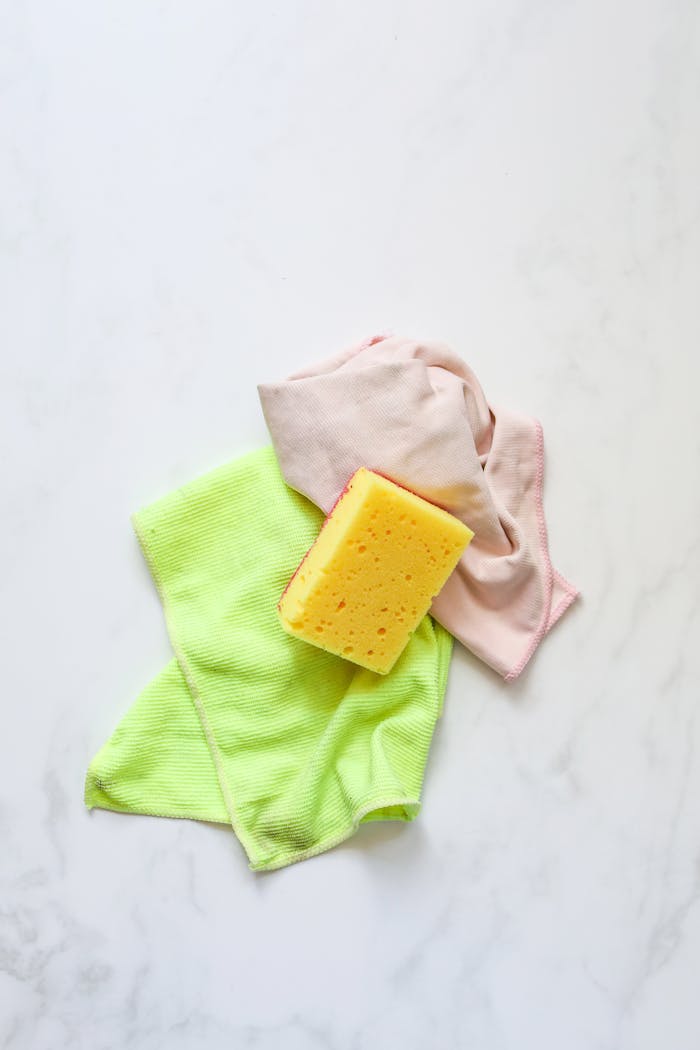 Colorful cleaning supplies with sponge on a marble surface, ideal for housekeeping themes.